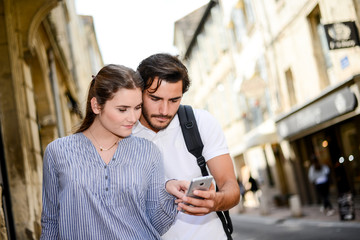 cheerful young couple using app on smartphone on a cultural weekend city trip discovering together historical european city in summer