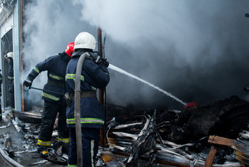 Firefighters spray water. Smoke and buiding after fire