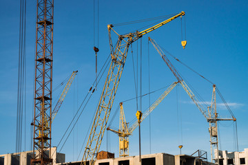 Big tower cranes above buildings under construction against blue sky. Background image of construction close-up with copy space. Build of city.