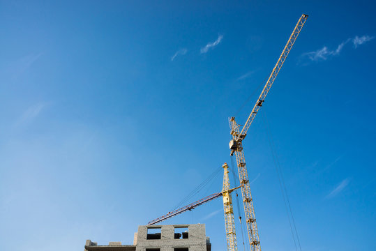 Big tower cranes above buildings under construction against blue sky. Background image of construction close-up with copy space. Build of city.