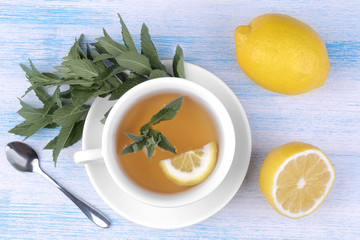 White cup of tea with mint and lemon on a blue wooden background top view