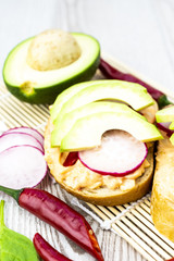 Bread with cheese spread, chili peppers, radishes and the sliced avocado on the wooden table. 