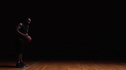 A basketball player takes a free throw on a darkly lit court - Powered by Adobe