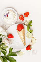 Strawberry ice cream on a white plate with white peonies, slices of lime, lemon, fresh strawberries and cakes.