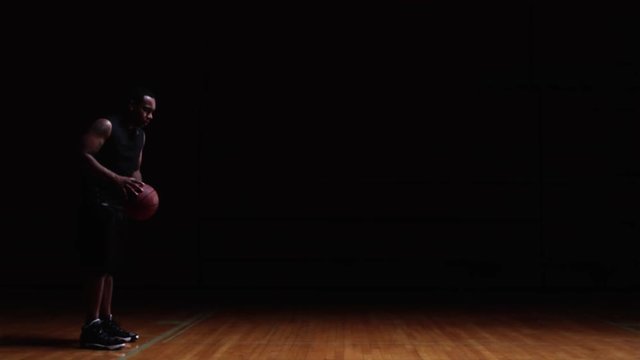 A basketball player takes a free throw on a darkly lit court