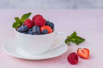 Fresh summer berries in the mug over the pink background