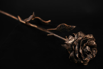 The rose with bloom and a stalk of bronze color made of metal, lies on a surface of black color