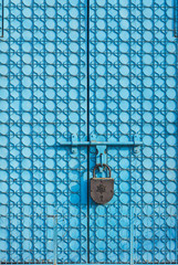 Big metal gate of blue color with patterns, are closed on the huge padlock with the image of a...