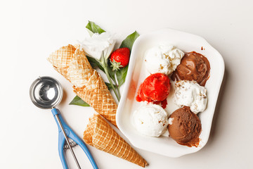 Ice cream balls with different tastes in a white plate on a table with leaves, strawberries, ice...