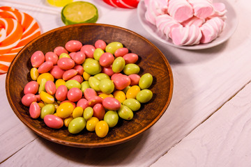 Ceramic plate with colored candies, lollipops and marshmallows on a wooden table