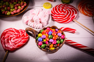 Fototapeta na wymiar Ceramic bowl with colored candies, lollipops and marshmallows on a wooden table