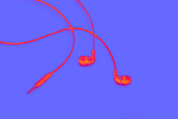 Red headphones for listening music and sound on portable devices and jack for connection on a blue background. Ear plugs.