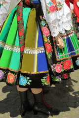 Tradycyjna pasiasty ludowy strój kobiety z Łowicza, widoczna kobieta od pasa w dół, pasiasta kolorowa wyszywany w kwiaty wełniana spódnica, biała koronkowa koszula, zapaska, dłoń, na ulicy - obrazy, fototapety, plakaty