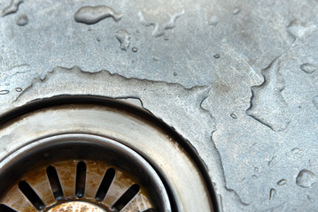 Dirty stainless steel sink drain close up with water drop.