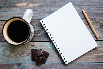 Cup of coffee, chocolate and a notebook with a pen on the table
