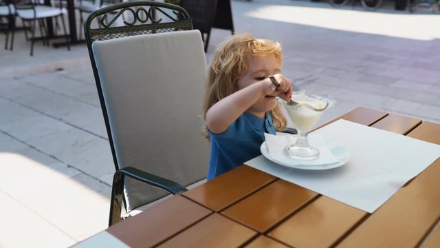 Kid eating ice cream in cafe. Funy curly child with icecream outdoor.