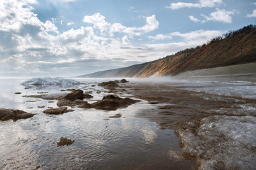 a misty spring morning on the snowy shore of a calm river overlooking the mountains