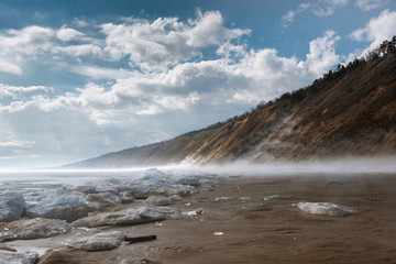 a misty spring morning on the snowy shore of a calm river overlooking the mountains