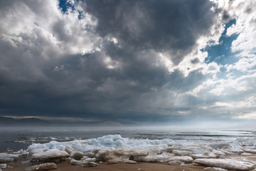 Obraz premium a misty spring morning on the snowy shore of a calm river overlooking the mountains