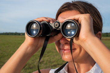 Woman use of the binoculars for looking up. She is walking near lake and watching birds or animals