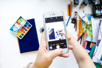 hand holding phone taking photo of Flat lay artist space