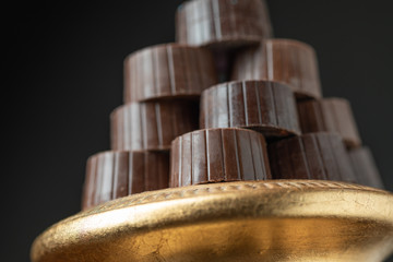 Stack of Fine Chocolates On Golden Pillar Dish With Dark Background