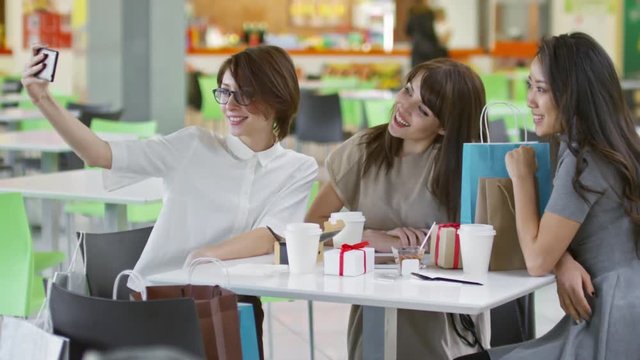 Medium shot of three young women taking selfie on smartphone camera when sitting in cafe after shopping