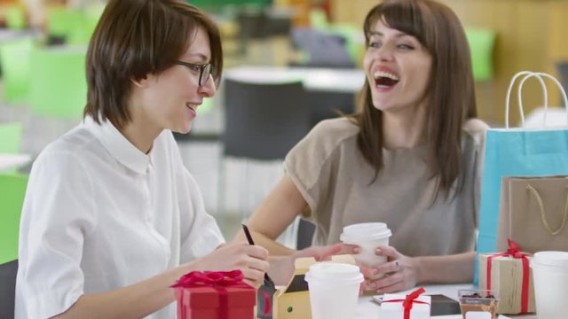 Medium shot of three young female friends sitting at table in cafe, talking to each other and eating desserts after shopping