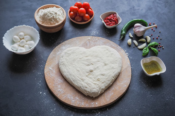 Heart-shaped dough and a set of ingredients for pizza on a black table. The view from the top.