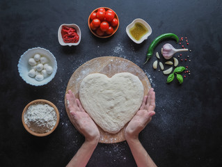 Heart-shaped dough and a set of ingredients for pizza on a black table. The view from the top.