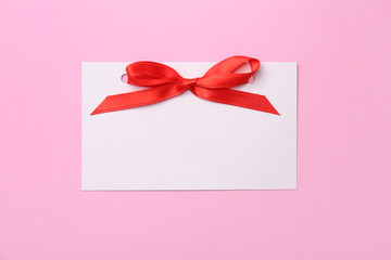 Blank gift tag with satin ribbon on color background, top view