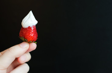 Summer fruit dessert: ripe red strawberry with whipped cream on top. Selective focus, black background