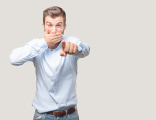 young handsome man joking and pointing front wearing a blue t shirt . person isolated against...