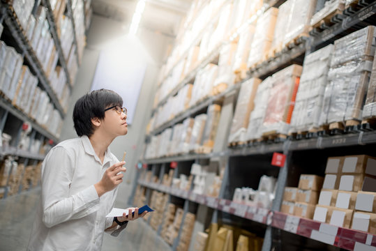 Young Asian man checking the shopping list and looking for product in warehouse wholesale, shopping warehousing concept