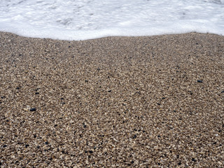 Wave, sea foam close-up on pebble beach