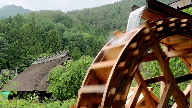 The mill wheel rotates under a stream of water, at village with traditional thatched roofed houses, Japan.