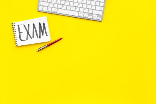 Exam concept. Lettering Exam in notebook on student's work desk on yellow backgrond top view copy space