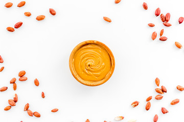 Product for hearty breakfast. High-calorie product. Peanut butter in bowl near nuts on white...
