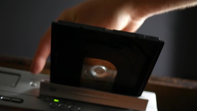 Person inserts a DVD laser disc into the DVD player and pushes it into the tray - low angle