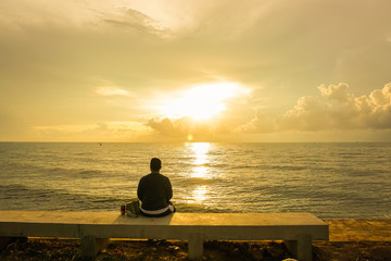 Man sitting at the seaside on a sunrise background.