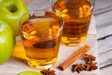 Apple juice in glasses, spices and apples on wooden cutting table 