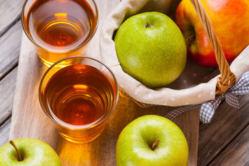 Apple juice in glasses and apples in a wicker basket on wooden table 