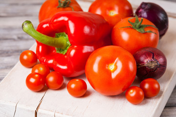 Cherry tomatoes, tomatoes, onion, bell pepper on wooden cutting board 