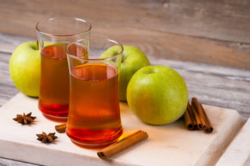 Apple juice in glasses, spices and apples on wooden cutting table 