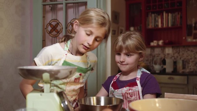 Young Kids who could be Sisters Baking a Cakre use Kitchen Scale to measure out the butter