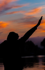 Vertical view of silhouette of a man at sunset with his hands up. Concept of victory