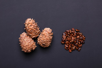 A handful of pine nuts in shells and cones on black background Three hole cedar cones Copy space Top view