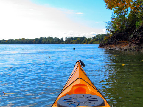 Bow of yellow kayak. Kayaking on peaceful calm river near shore at sunny autumn day. Shot from point of view of the paddler.