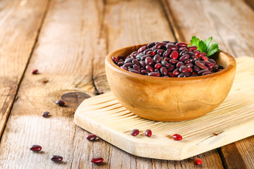 Red raw beans with greens on a wooden table.