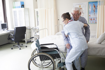 Fototapeta na wymiar 介護士が、リハビリ中の老人を車椅子に座らせている。